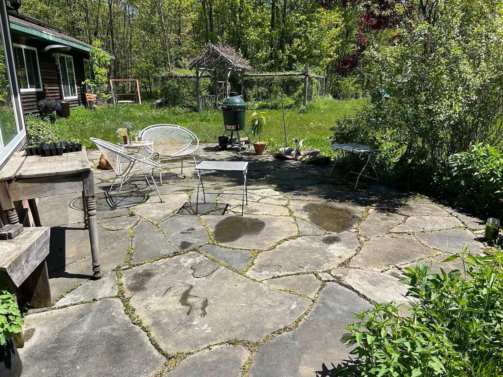 The stone patio has a southern exposure and looks west to the flower and berry garden and, beyond that, the little pond. There is a Big Green Egg smoker and barbecue grill on the patio.